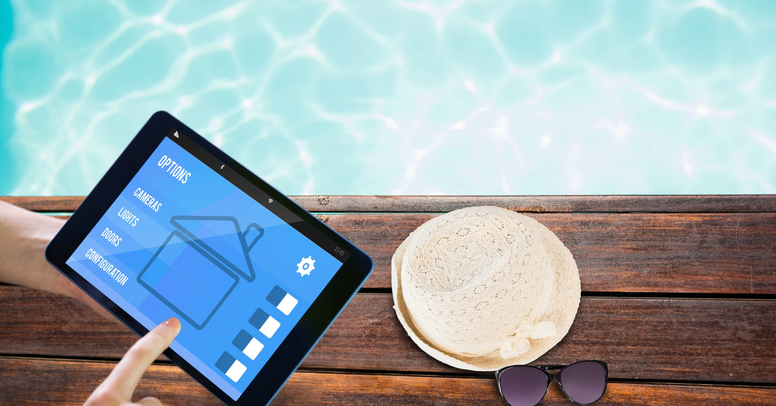 A Hand Using A Tablet To Manage Facility Options Next To A Pool Deck With A Sun Hat And Sunglasses